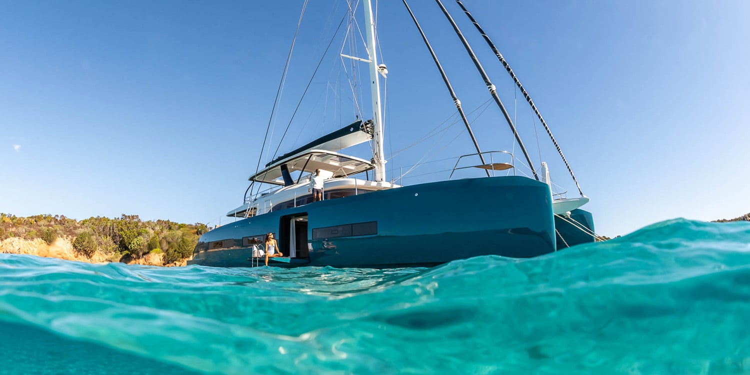 Lagoon Eighty 2 catamaran with teal hull at anchor in turquoise water, seen from the waterline
